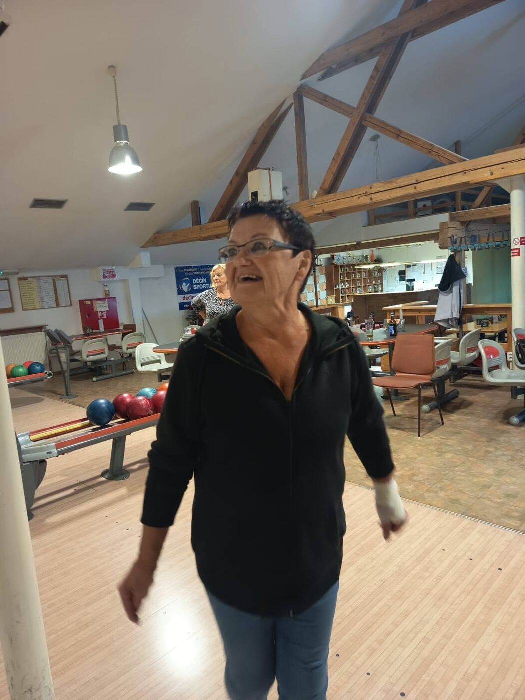 Usměvavá žena v bowlingové herně, v pozadí koule a stoly